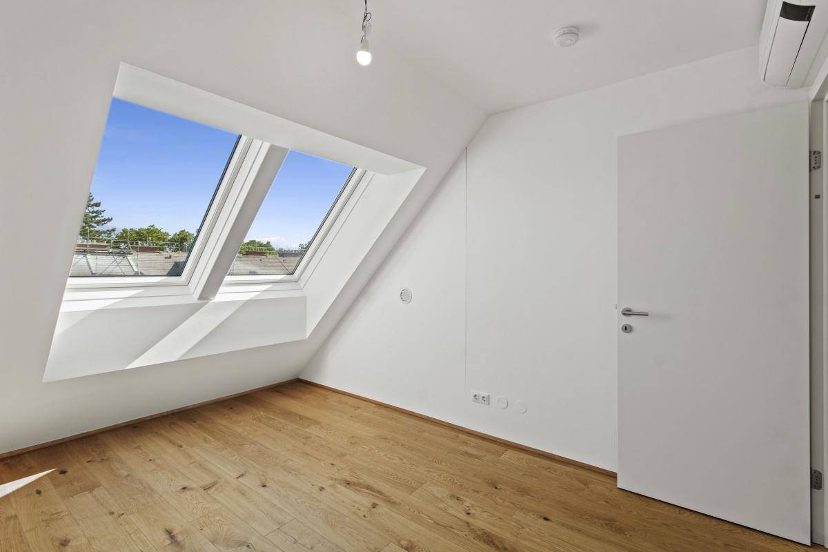 Lichtdurchflutetes Dachgeschosszimmer mit Parkettboden, Klimaanlage und Dachfenstern.