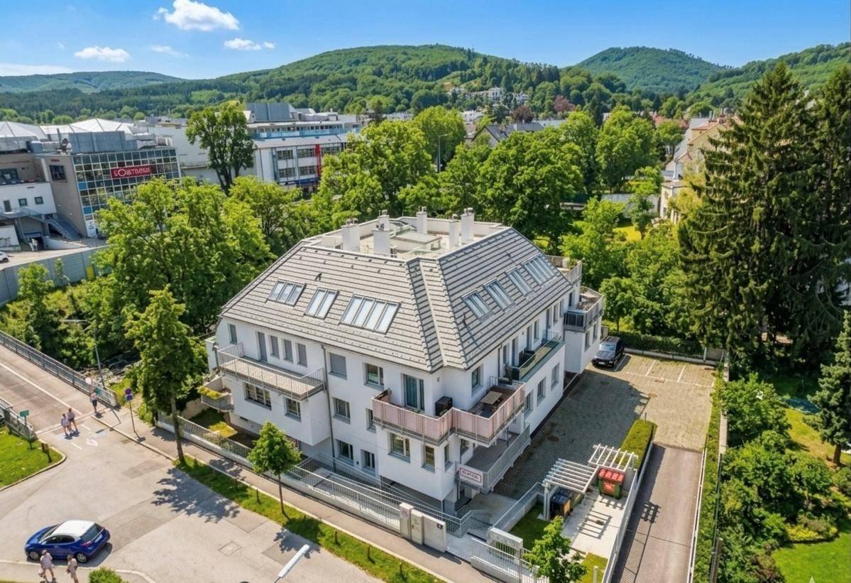 Luftaufnahme des Wohngebäudes mit umliegender Infrastruktur und viel Grün, unter blauem Himmel.