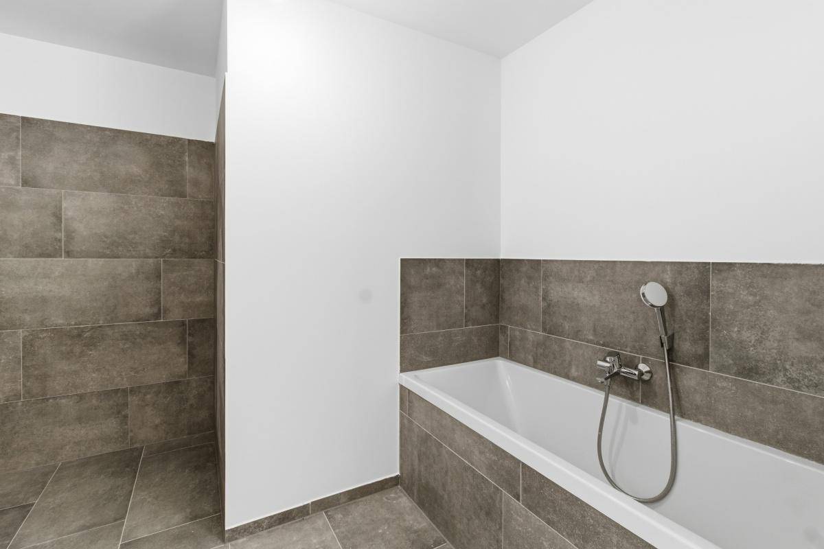 Modernes Badezimmer mit Badewanne und Duschbereich, ausgestattet mit grauen Fliesen.