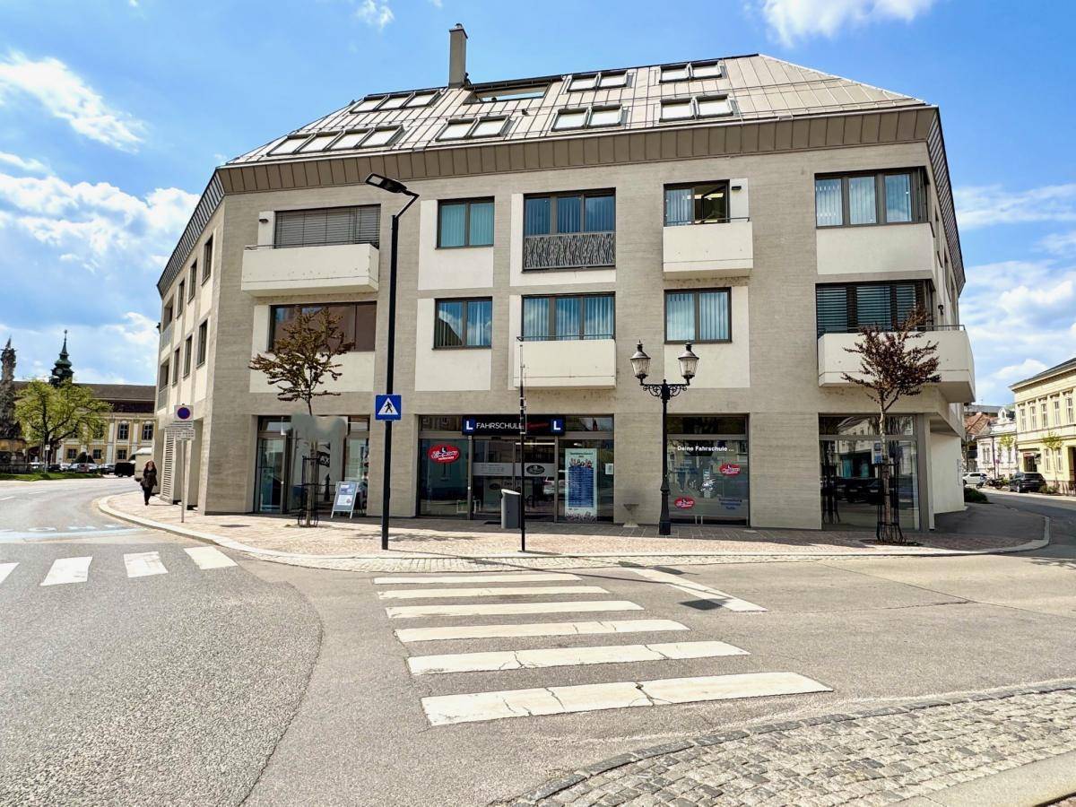 Modernes Eckgebäude mit Geschäften im Erdgeschoss und Wohnungen darüber, an einer städtischen Kreuzung gelegen.