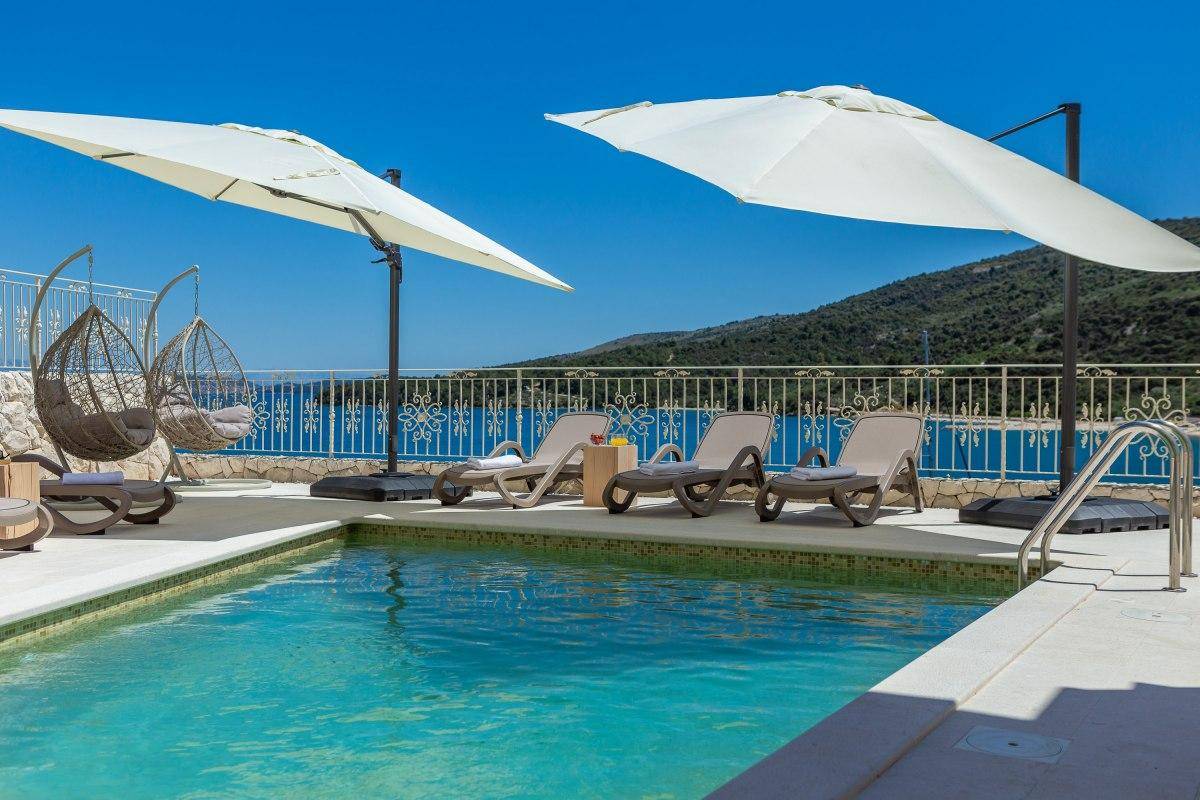 Großzügiger Poolbereich mit Sonnenschirmen, Hängesesseln und Panoramablick auf das Meer.