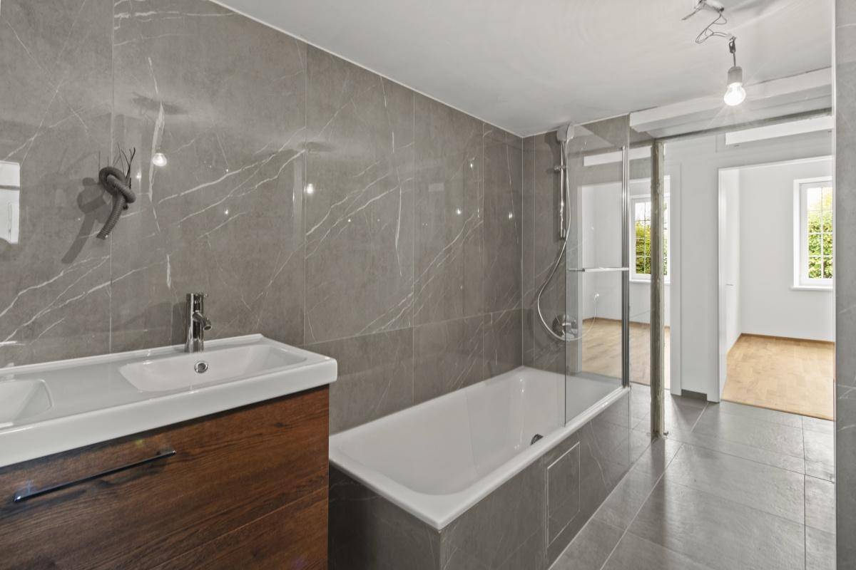 Elegantes Badezimmer mit grauen Marmorfliesen, Waschtisch und Badewanne mit Duschabtrennung.