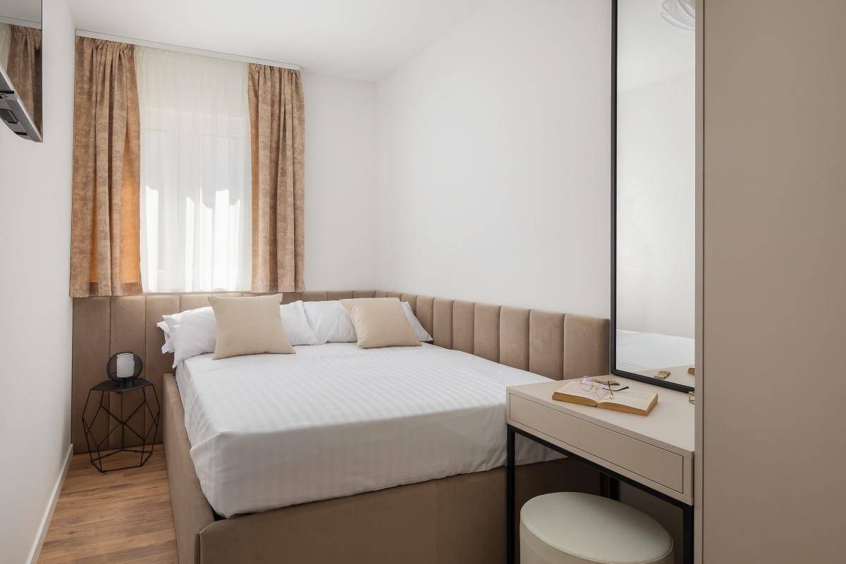 Helles Schlafzimmer mit Einzelbett, integriertem Schminktisch und Spiegel, sowie Holzboden.
