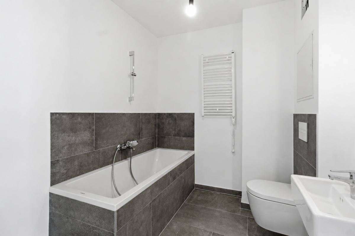 Modernes Badezimmer mit Badewanne, Wand-WC, Waschbecken und beheiztem Handtuchhalter.