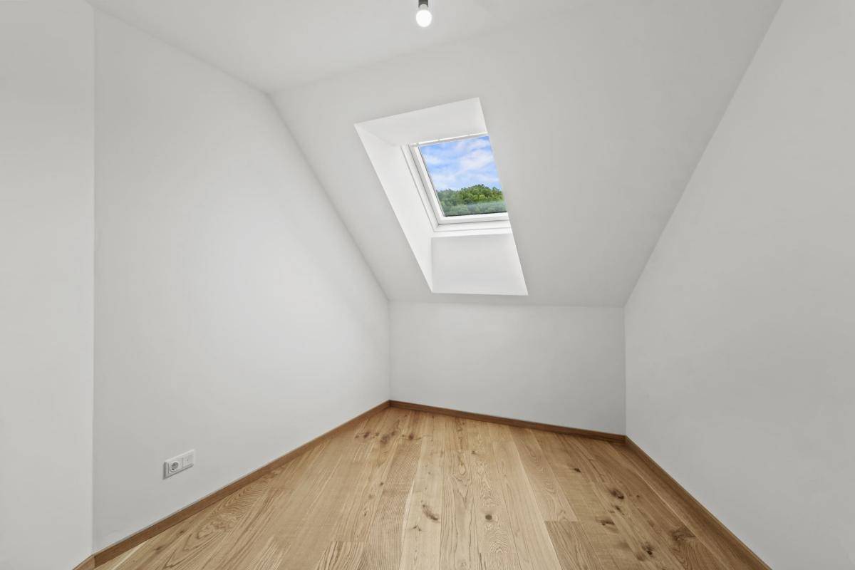 Helles Zimmer mit Holzboden, Dachschräge und einem Dachfenster, perfekt für ein Arbeitszimmer.