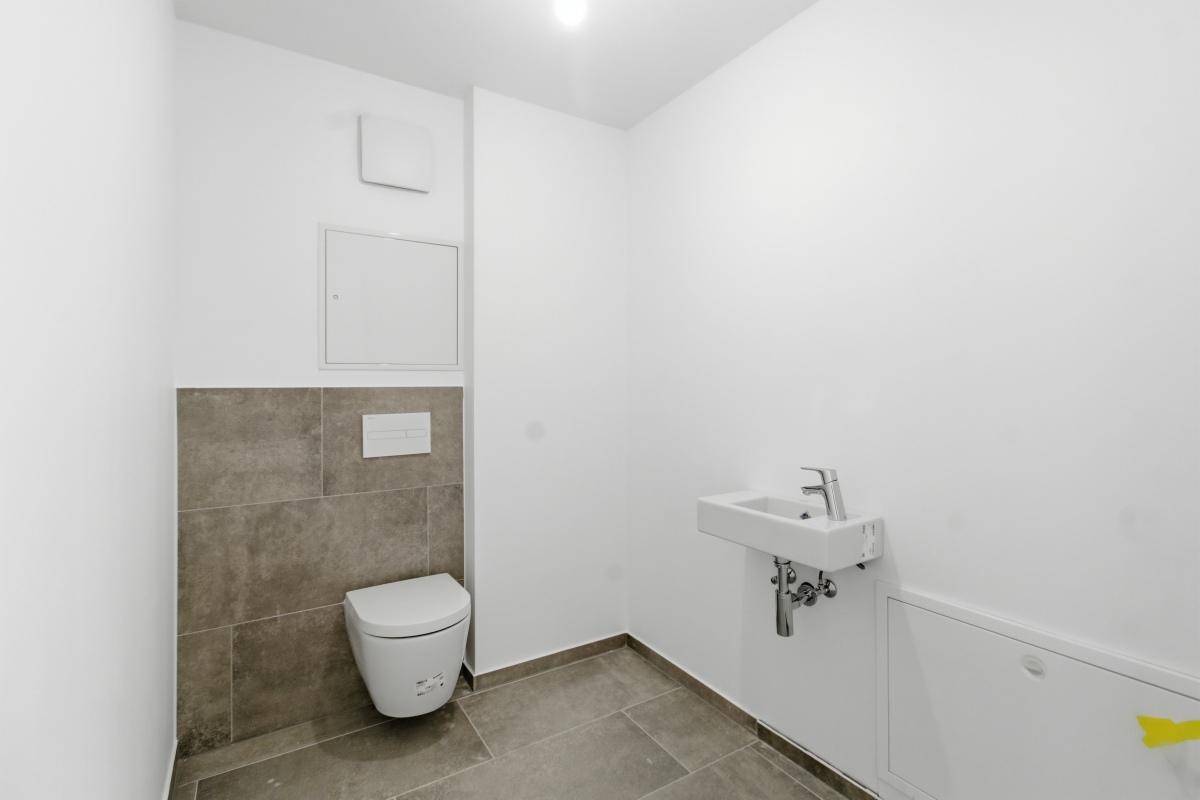 Modernes Gäste-WC mit wandhängender Toilette, kleinem Waschbecken und grauen Fliesen.