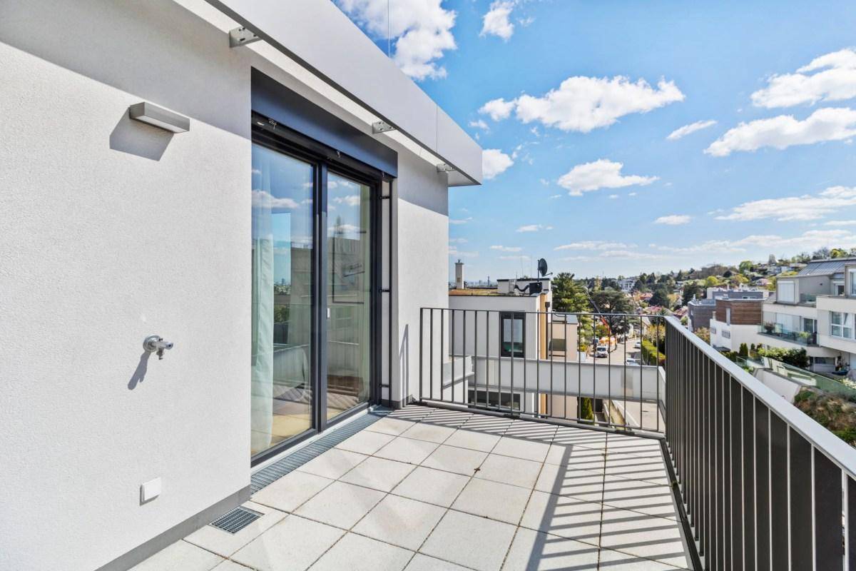 Kleiner Balkon mit Fliesenboden und Blick auf die umliegenden Gebäude und grünen Hügel.