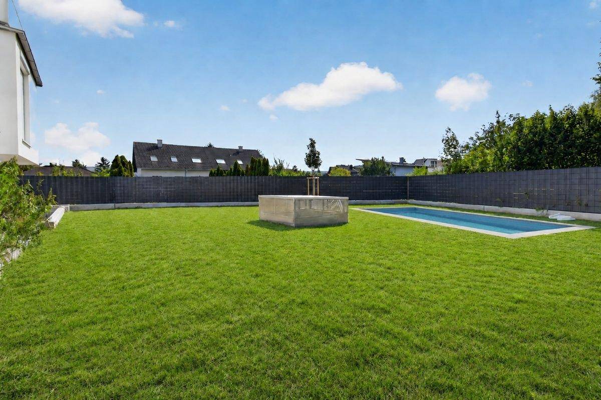 Weitläufiger Garten mit Rasenfläche und einem rechteckigen Swimmingpool.