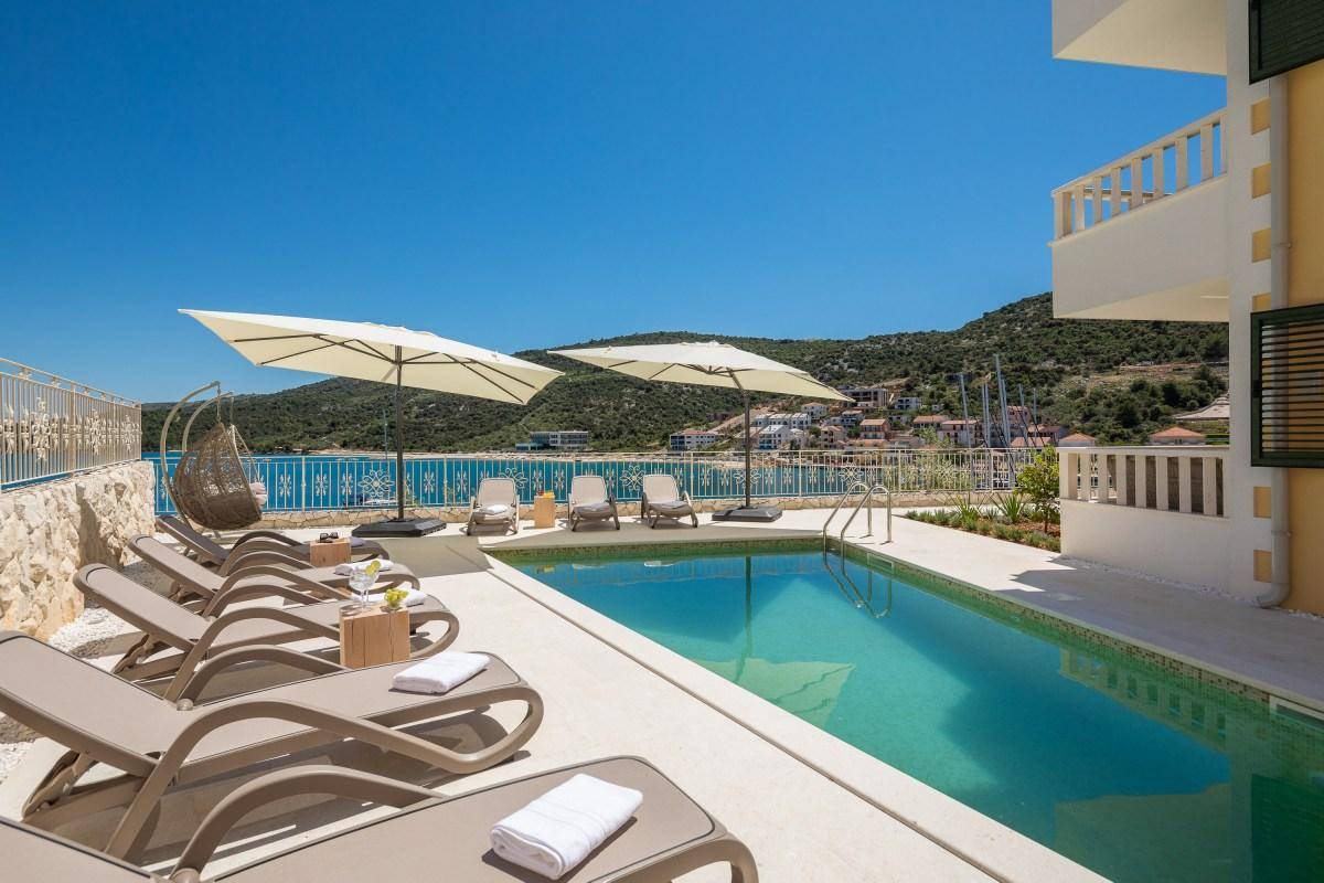 Heller Poolbereich mit vielen Liegestühlen, Sonnenschirmen und atemberaubendem Meerblick.
