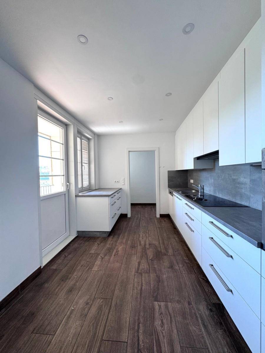 Moderne Küche mit weißen Schränken, dunklen Arbeitsplatten und Zugang zu einem Balkon.