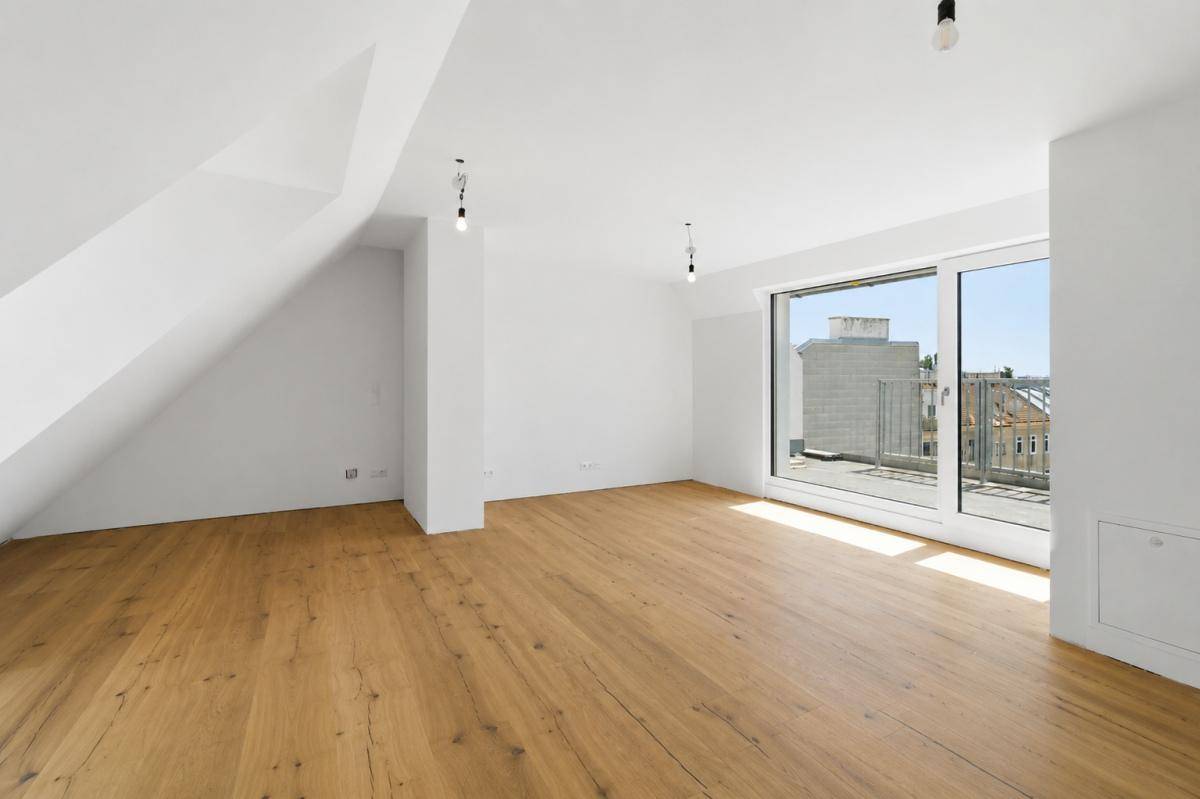 Geräumiger, heller Dachgeschossraum mit Holzboden und großen Fenstern, die viel Tageslicht hereinlassen.