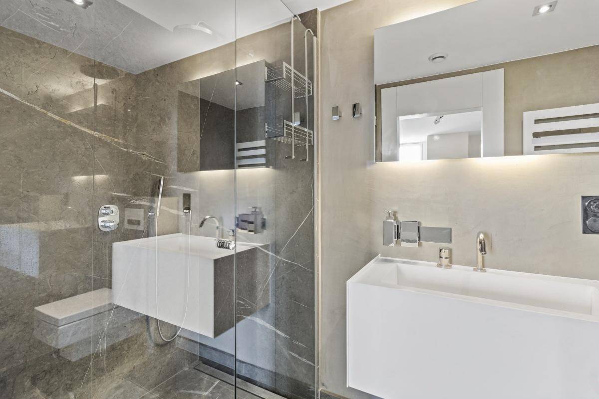 Modernes Badezimmer mit schwebenden Waschbecken, großer Dusche und Marmorwänden.