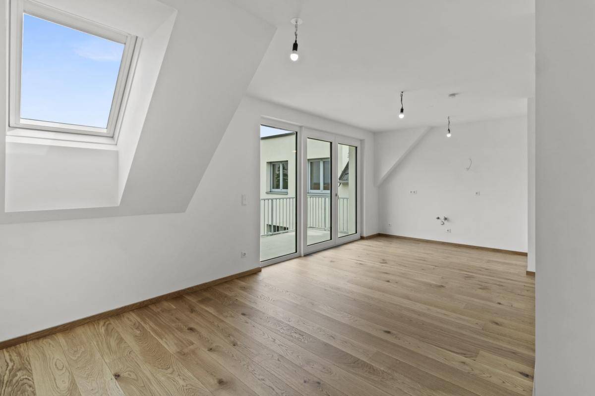 Heller Wohnraum mit Holzboden, Balkonzugang, Dachschräge und einem Oberlichtfenster.