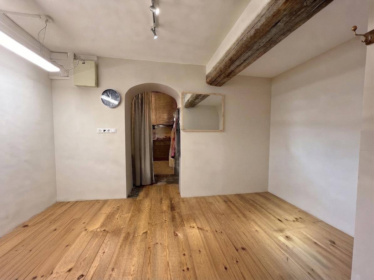 Raum mit Holzdielenboden, freiliegenden Holzbalken und einem bogenförmigen Durchgang zu einem hinteren Bereich.