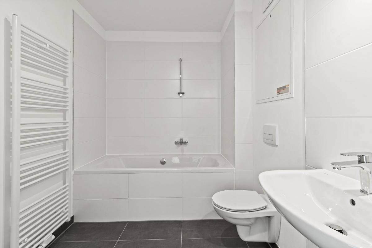 Helles Badezimmer mit Badewanne, wandhängendem WC, Einzelwaschbecken und Handtuchheizkörper.