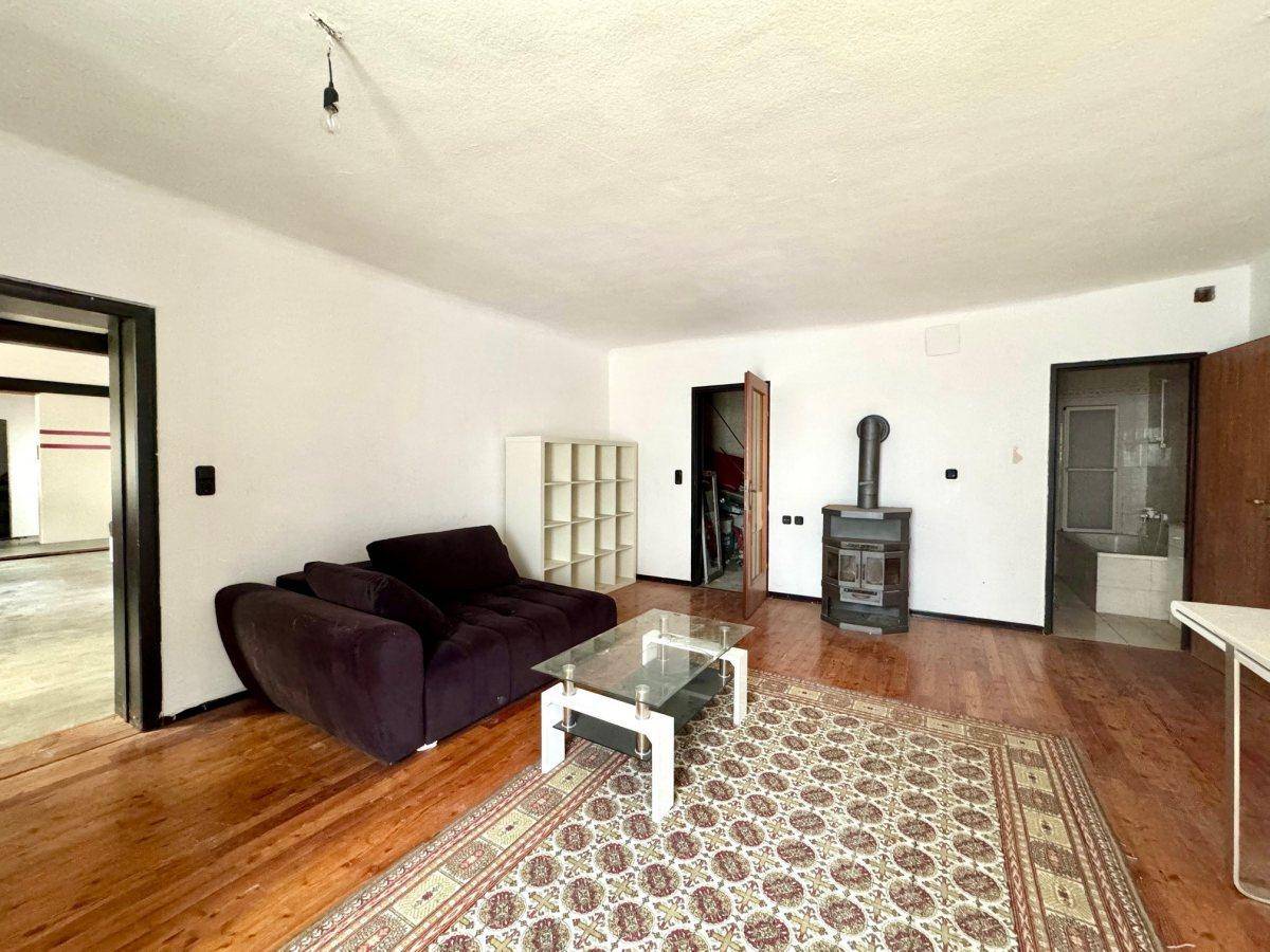 Gemütliches Wohnzimmer mit Holzboden, Sofa, Teppich und einem traditionellen Holzofen.