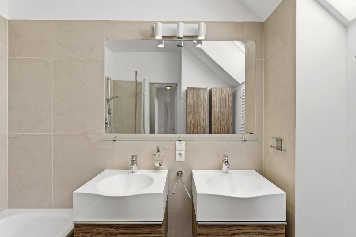Elegantes Badezimmer mit Doppelwaschbecken, großem Spiegel und beigefarbenen Wandfliesen.