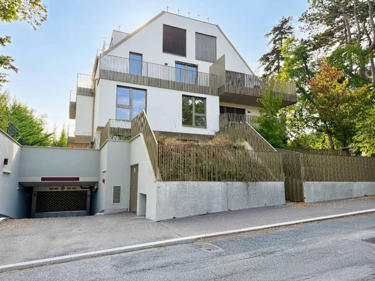 Modernes Mehrfamilienhaus mit weißer Fassade, Balkonen und Tiefgaragenzufahrt in grüner Umgebung.