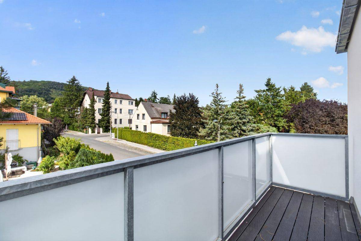 Balkon mit Holzdielen und weitem Blick über die grüne Umgebung und die umliegenden Häuser.