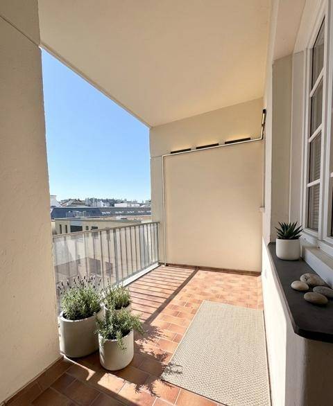 Heller Balkon mit Terrakottafliesen, Topfpflanzen und einem weiten Blick über die Dächer der Stadt.