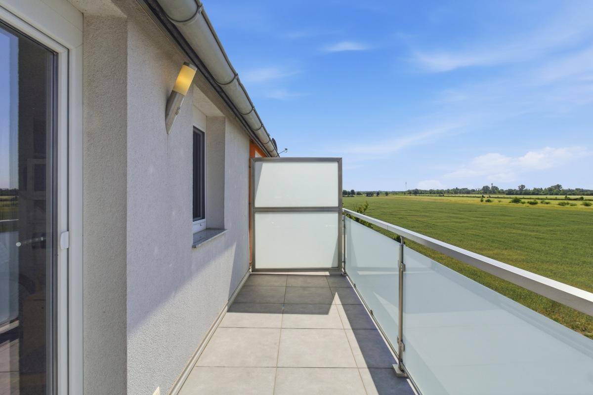 Heller Balkon mit Fliesenboden und Glasgeländer, bietet einen weiten Blick über grüne Felder.