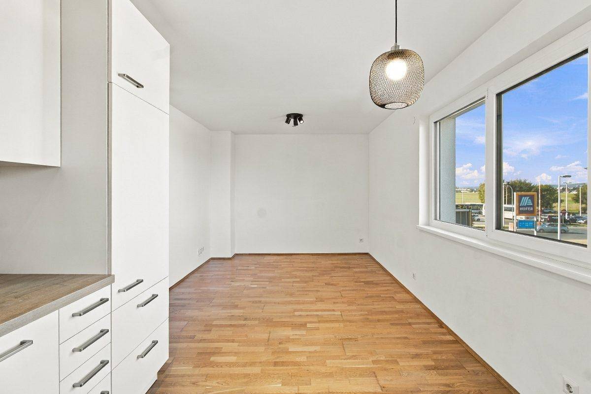 Heller Raum mit Holzboden und großem Fenster, das einen Blick auf die Umgebung bietet.