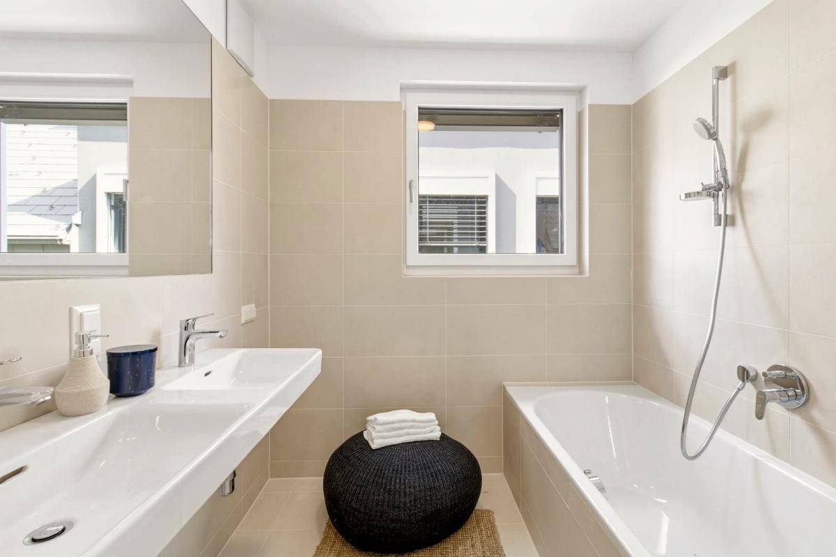 Helles Badezimmer mit Doppelwaschbecken, Badewanne und Fenster.