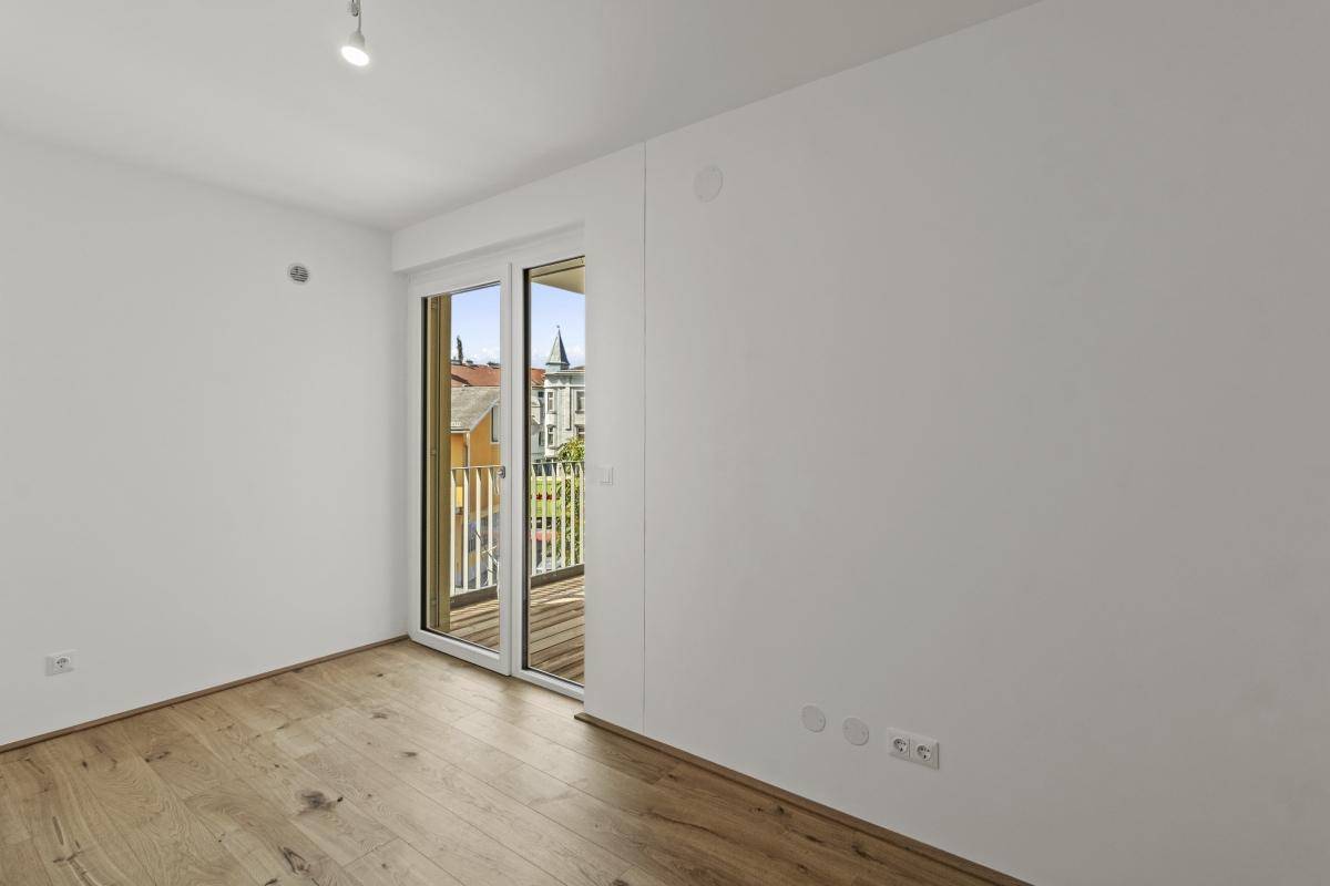 Helles Schlafzimmer mit Parkettboden und französischem Balkon mit Stadtblick.