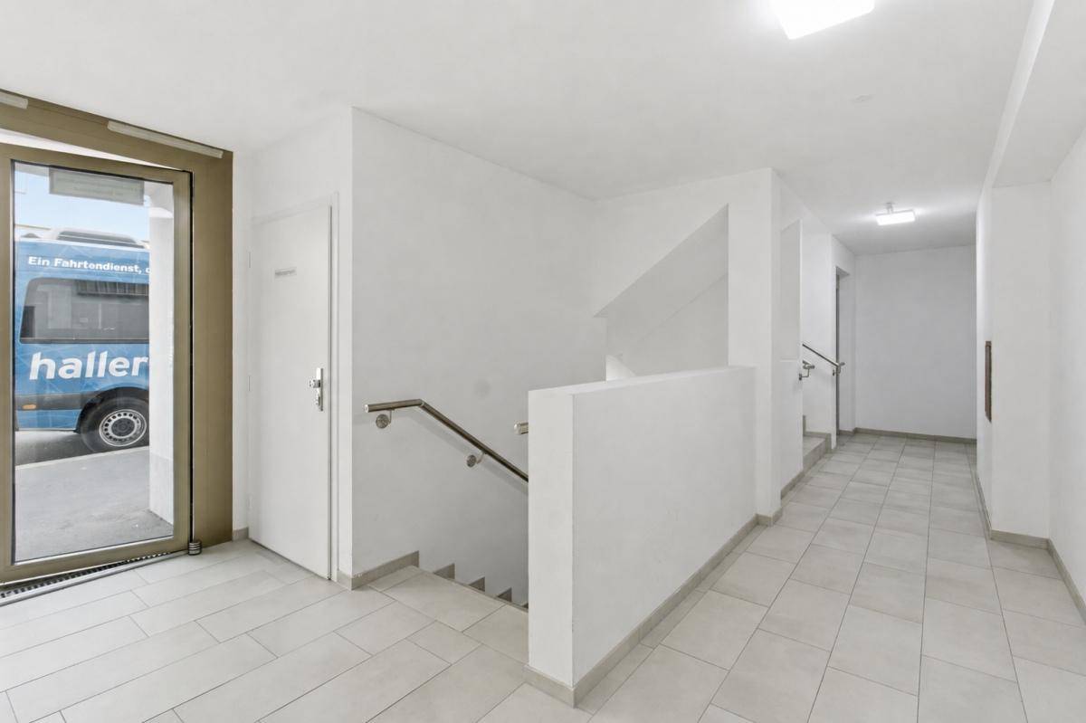 Heller Eingangsbereich mit Treppe und Rampe, ausgestattet mit hellen Fliesen.