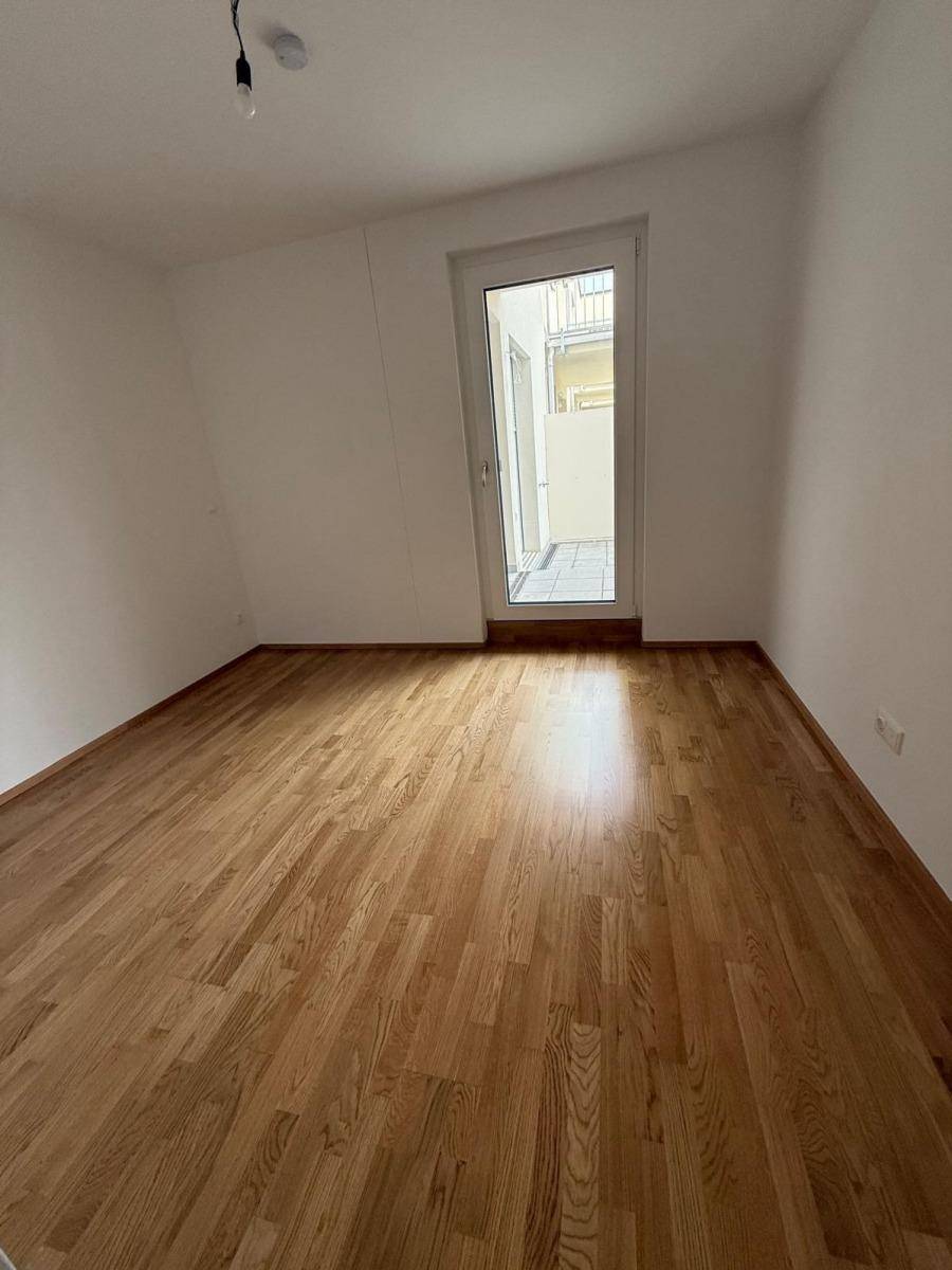 Helles Zimmer mit Holzboden und Fenstertür, die viel Tageslicht hereinlässt.