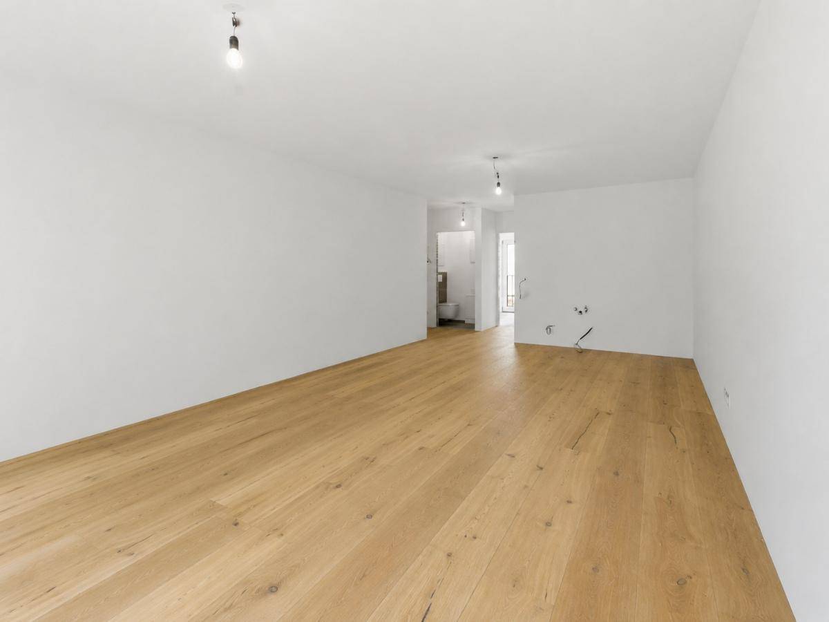 Leerer Raum mit hellem Holzparkett und Blick in einen angrenzenden Sanitärbereich.