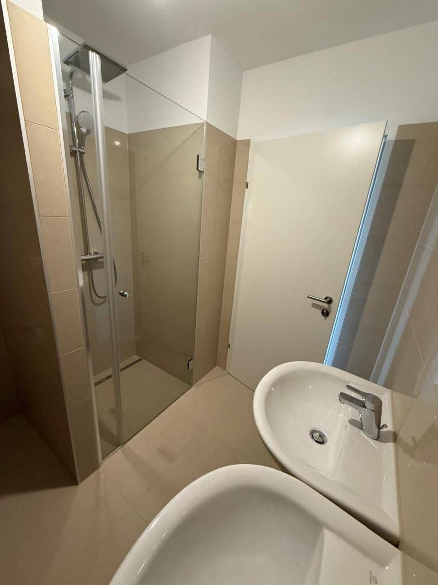 Helles Badezimmer mit Duschkabine, Waschbecken und beigefarbenen Wandfliesen.