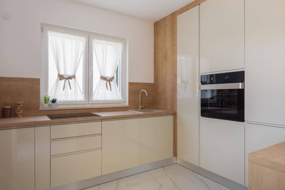 Funktionale Küche mit hellen Schränken, Holzarbeitsplatte und integriertem Backofen, gut beleuchtet durch ein Fenster.