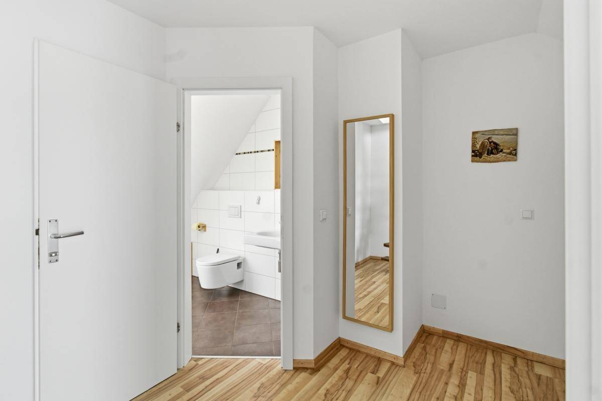 Heller Flur mit Holzboden und einem Ganzkörperspiegel, der zum Badezimmer führt.