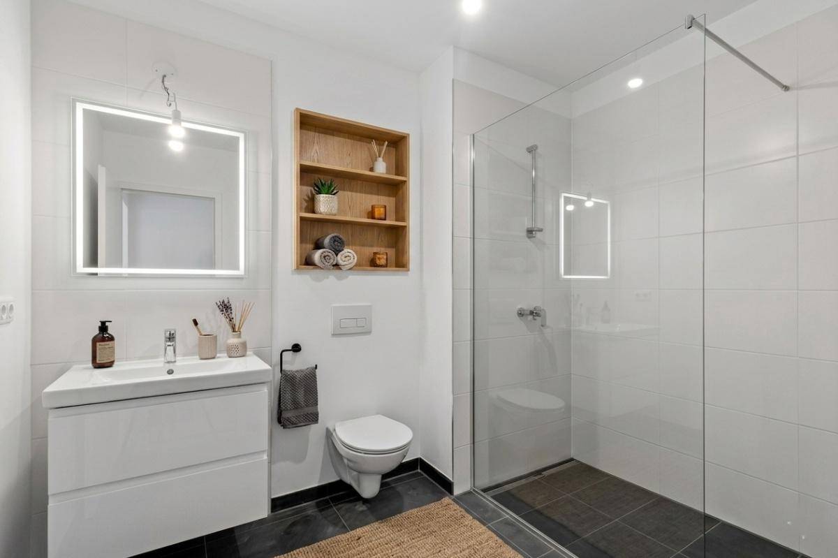 Modernes Badezimmer mit begehbarer Dusche, Wand-WC und beleuchtetem Spiegel.