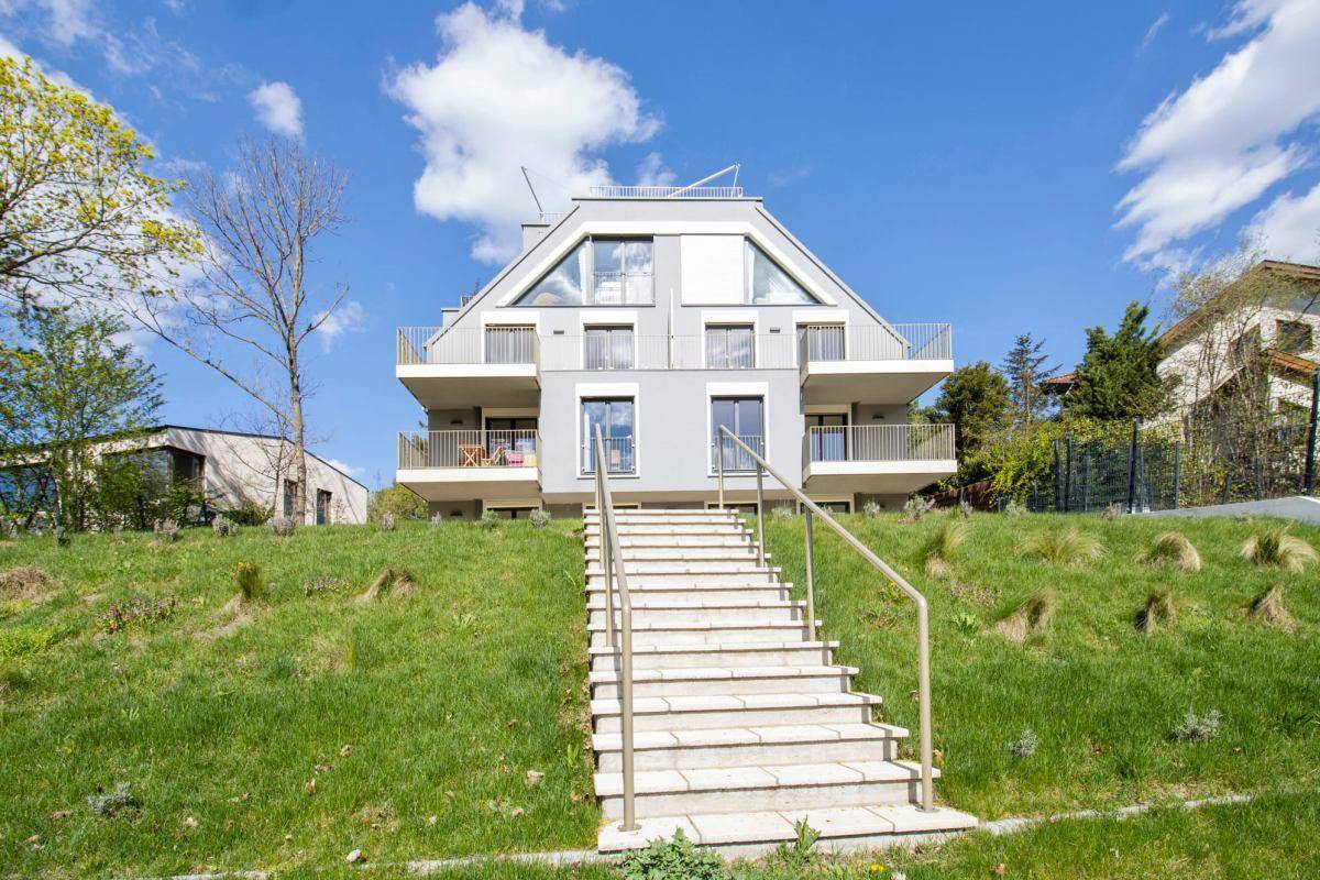 Modernes Apartmentgebäude auf einem grünen Hügel mit einer Steintreppe, die zum Eingang führt.
