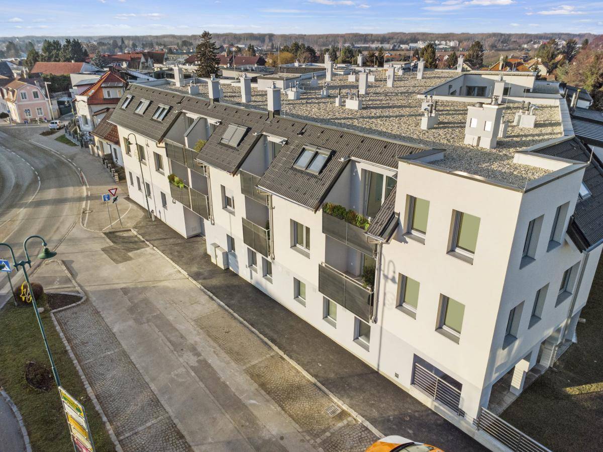 Seitenansicht des modernen Neubaus mit Balkonen und Dachgauben in einer ruhigen Straße.