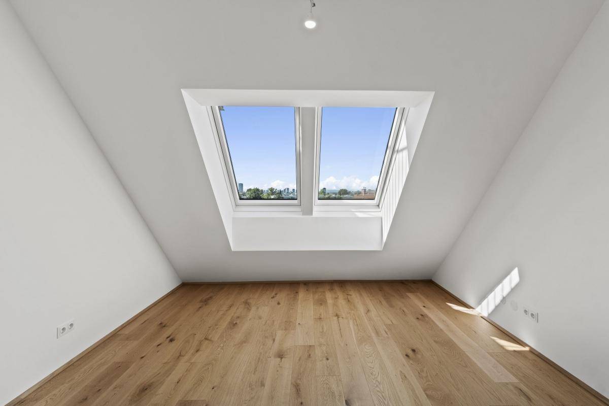 Helles Zimmer im Dachgeschoss mit Holzboden und zwei großen Dachfenstern.