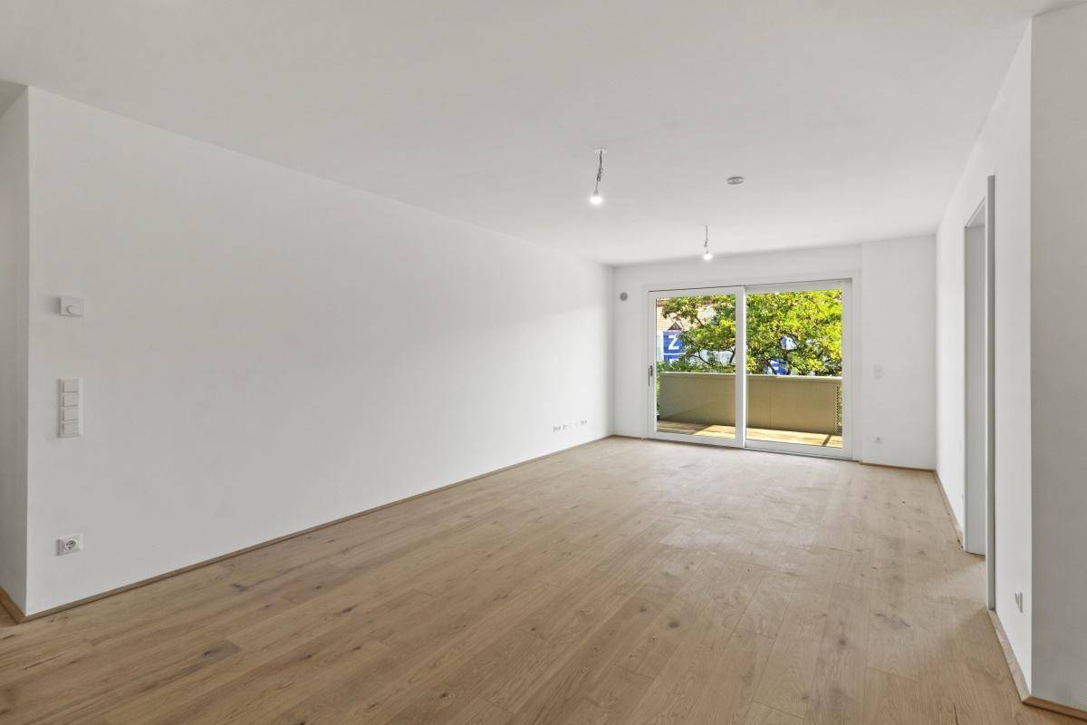 Heller, leerer Raum mit Eichenparkettboden und großem Schiebetürzugang zu einem Balkon.