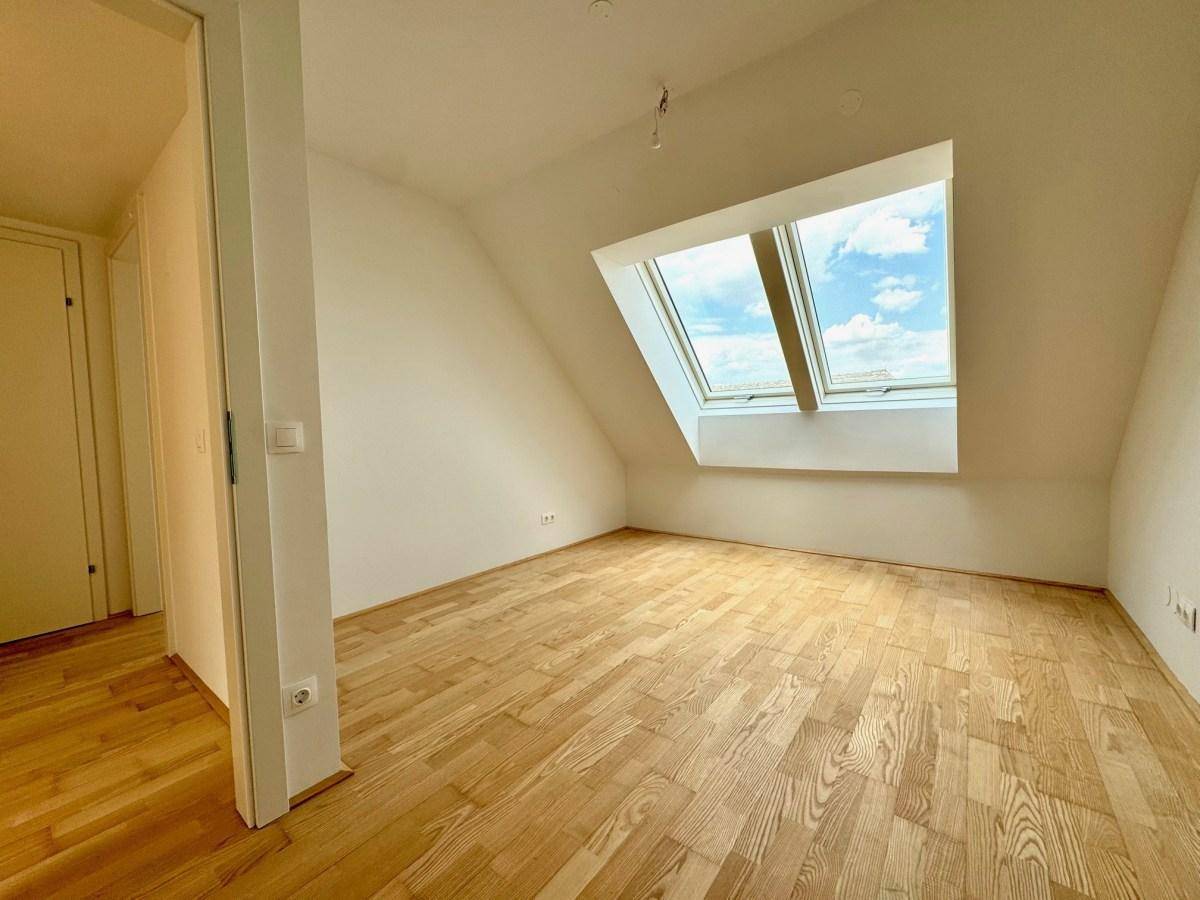 Heller Dachgeschossraum mit Holzboden und großen Dachfenstern, die viel Licht hereinlassen.