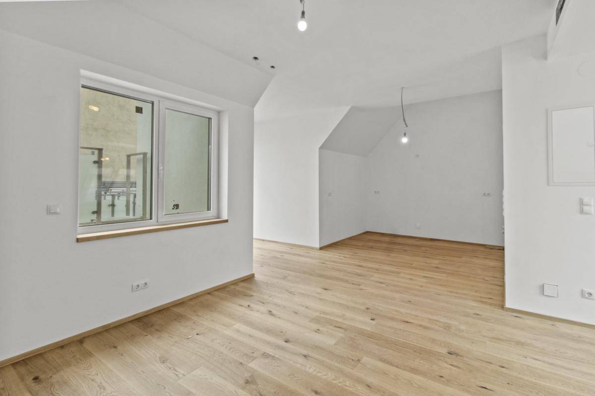 Helles Zimmer mit Holzboden und schrägen Wänden, ausgestattet mit einem Fenster für Tageslicht.