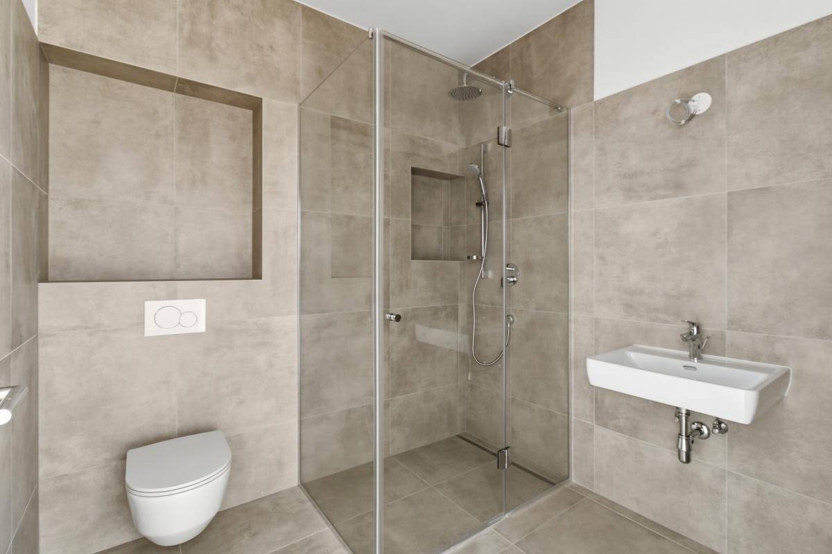 Modernes Badezimmer mit beigefarbenen Fliesen, wandhängendem WC und einer geräumigen Glasdusche.