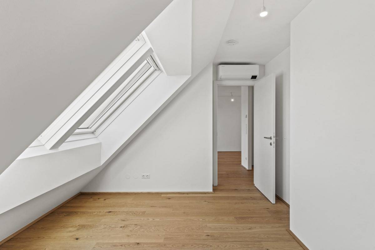 Lichtdurchflutetes Zimmer im Dachgeschoss mit Parkettboden und großem Dachfenster.