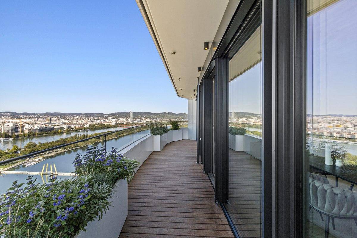 Lange Terrasse mit Holzdeck und raumhohen Glasfronten, die einen Panoramablick auf die Stadt freigeben.