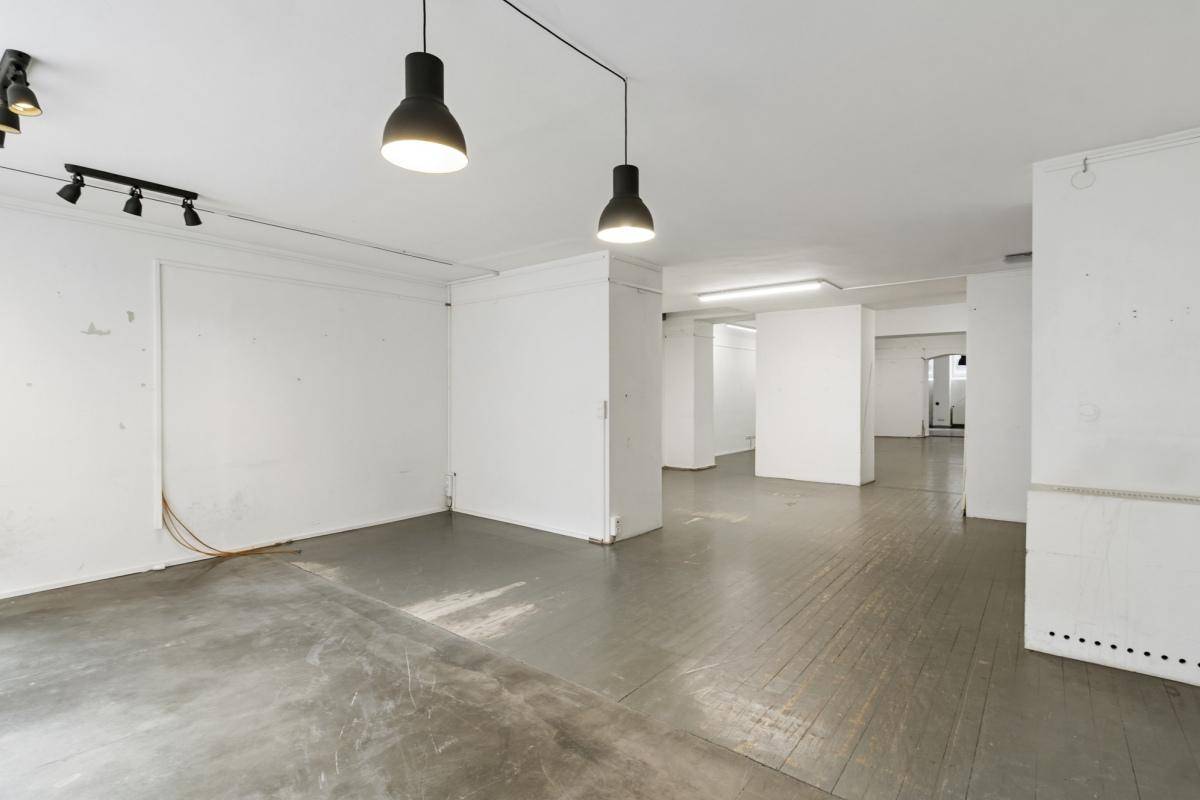 Großer, leerer Gewerberaum mit grauem Holzboden und modernen Hängelampen, helle Beleuchtung.