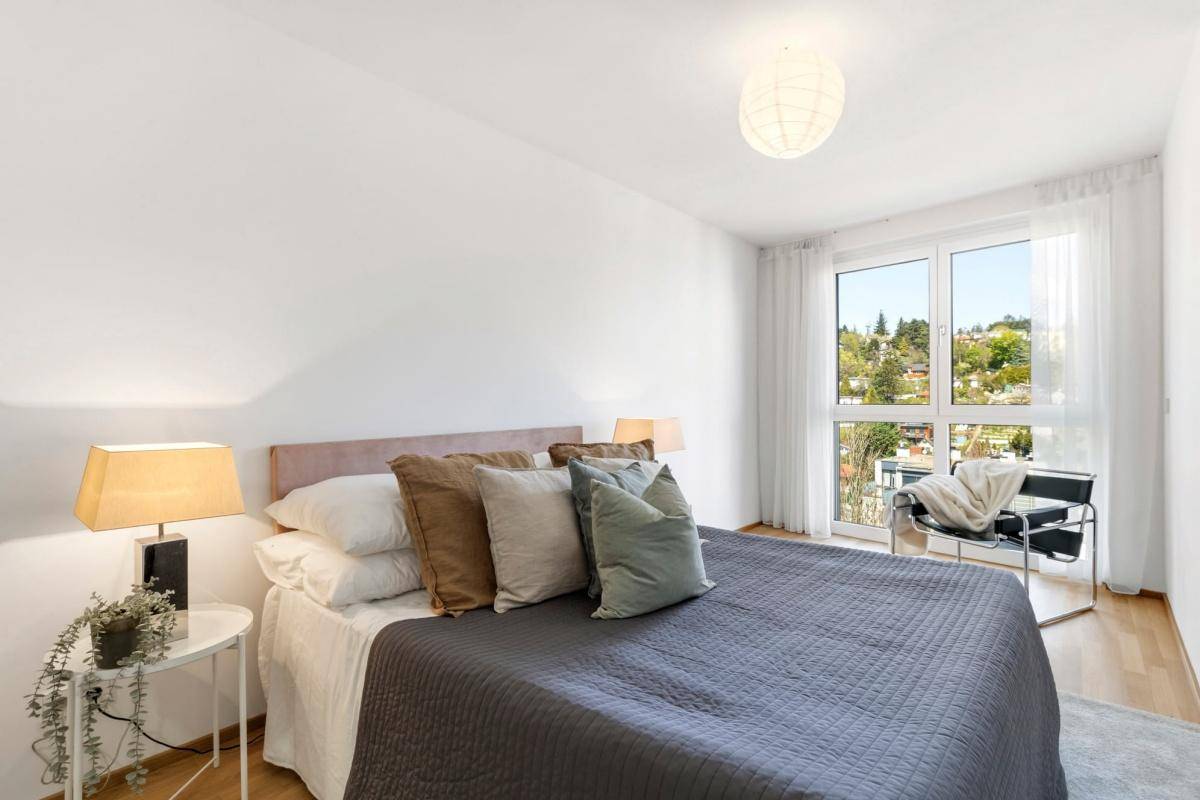 Gemütliches Schlafzimmer mit großem Bett, Parkettboden und Blick ins Grüne durch das Fenster.