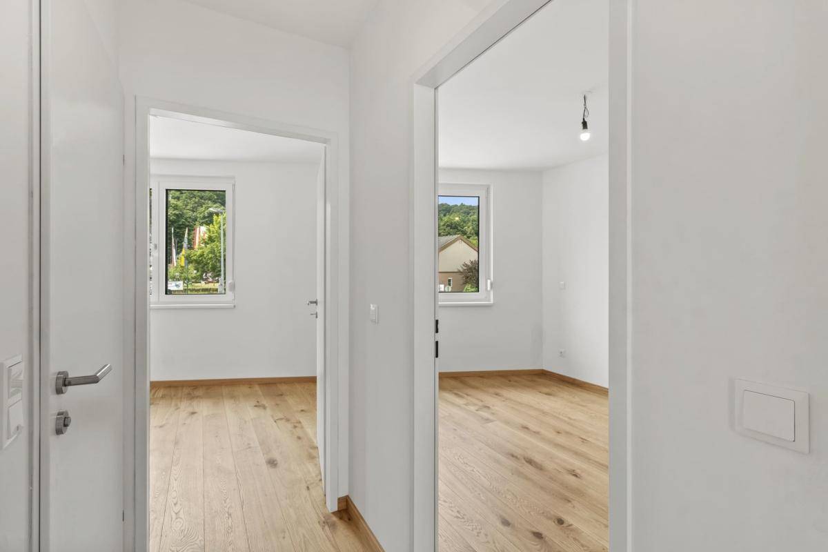 Blick vom Flur in zwei helle Zimmer mit Parkettboden und Fenstern.