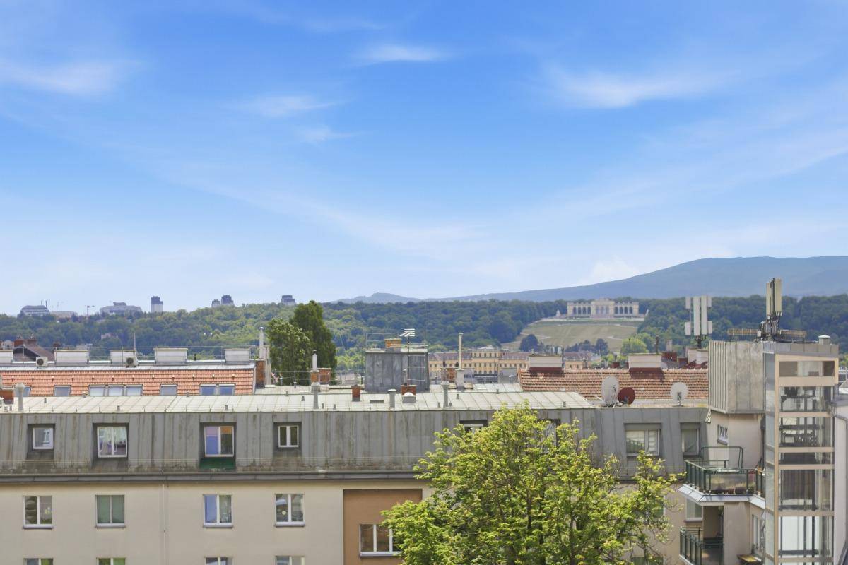 Weitläufiger Blick über die Dächer der Stadt mit grünen Hügeln und einem historischen Gebäude im Hintergrund.