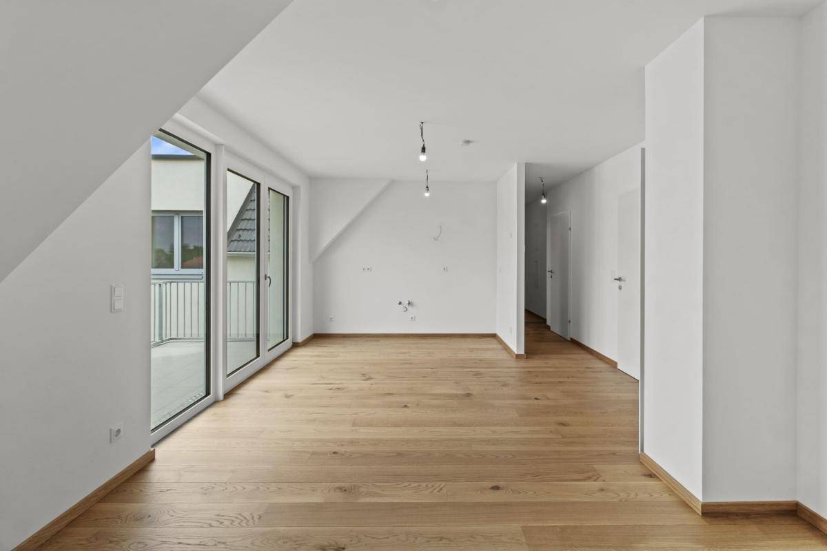 Heller Wohnbereich mit Holzboden, Dachschräge und großen Fenstern zum Balkon.