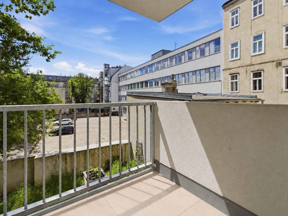Blick vom Balkon auf den Innenhof mit Parkplätzen und umliegenden Gebäuden unter blauem Himmel.